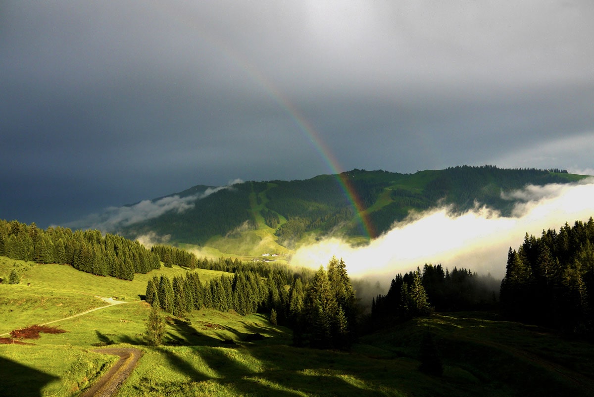 Eine Bergwiese mit einem Regenbogen und Wolken